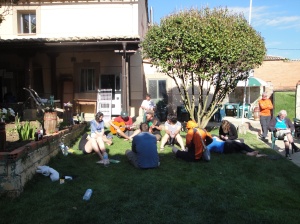 Young pilgrims from all over the world gathering to listen to two people strumming their guitars and singing in the garden/courtyard at the Jacque de Molay Alberque